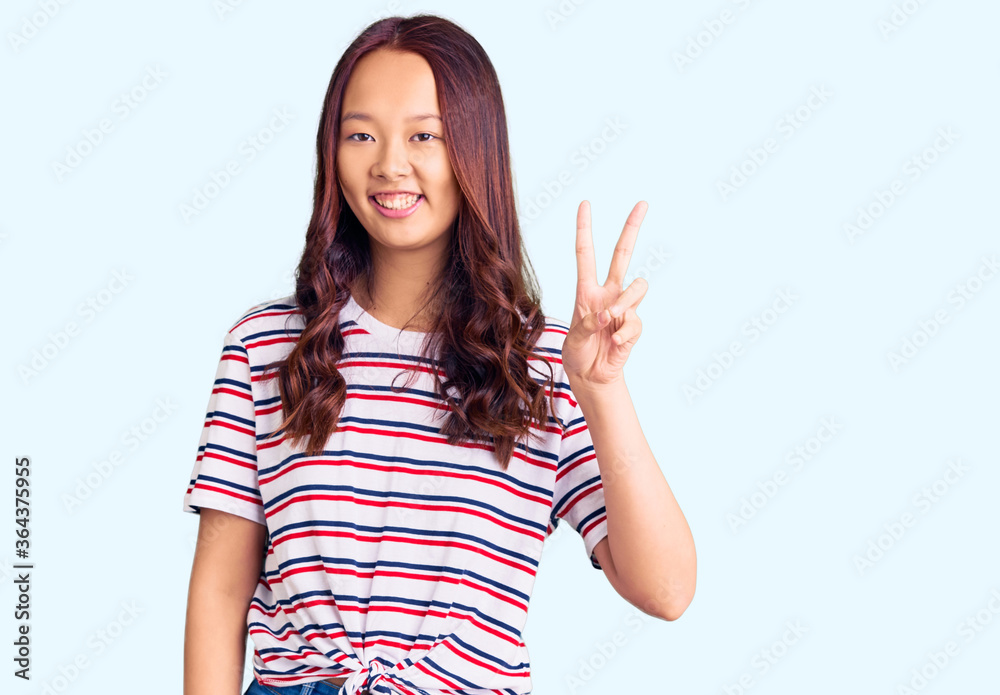 Young beautiful chinese girl wearing casual clothes smiling with happy face winking at the camera doing victory sign. number two. Young beautiful chinese girl wearing casual clothes smiling with happy face winking at the camera doing victory sign. number two.