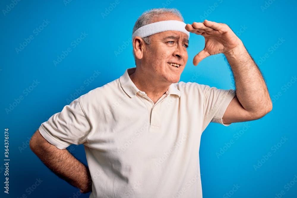 Middle age hoary sportsman doing sport wearing sportswear over isolated blue background very happy and smiling looking far away with hand over head. Searching concept.