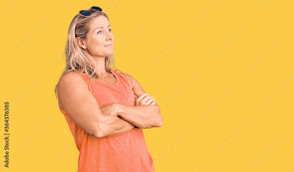 Obraz premium Middle age fit blonde woman wearing casual summer clothes and sunglasses looking to the side with arms crossed convinced and confident