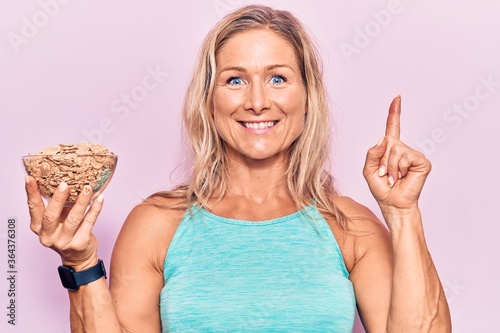 Middle age caucasian blonde woman holding bowl of healthy cornflakes surprised with an idea or question pointing finger with happy face, number one