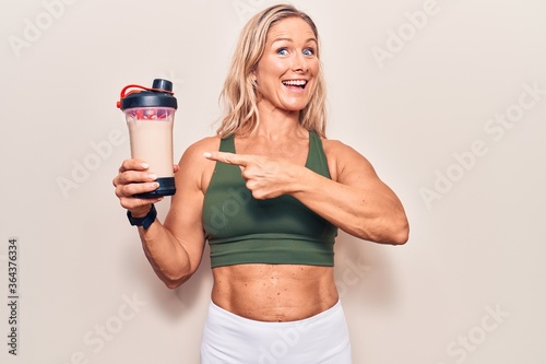 Middle age caucasian blonde woman wearing sport clothes drinking a protein shake smiling happy pointing with hand and finger © Krakenimages.com