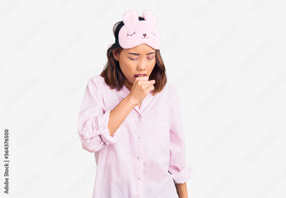 Young beautiful chinese girl wearing sleep mask and pajama feeling unwell and coughing as symptom for cold or bronchitis. health care concept. Young beautiful chinese girl wearing sleep mask and pajama feeling unwell and coughing as symptom for cold or bronchitis. health care concept.