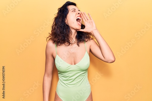 Young beautiful hispanic woman wearing swimwear shouting and screaming loud to side with hand on mouth. communication concept.