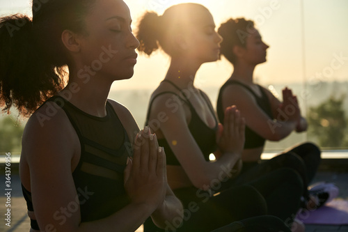 Fotografie Calm serene sporty young african american ethnic woman meditate sit namaste eyes closed doing breathing exercises practice relaxing at outdoor group multiethnic yoga class in morning sunrise light