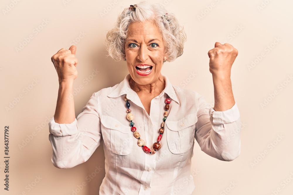 Obraz premium Senior grey-haired woman wearing casual clothes screaming proud, celebrating victory and success very excited with raised arms