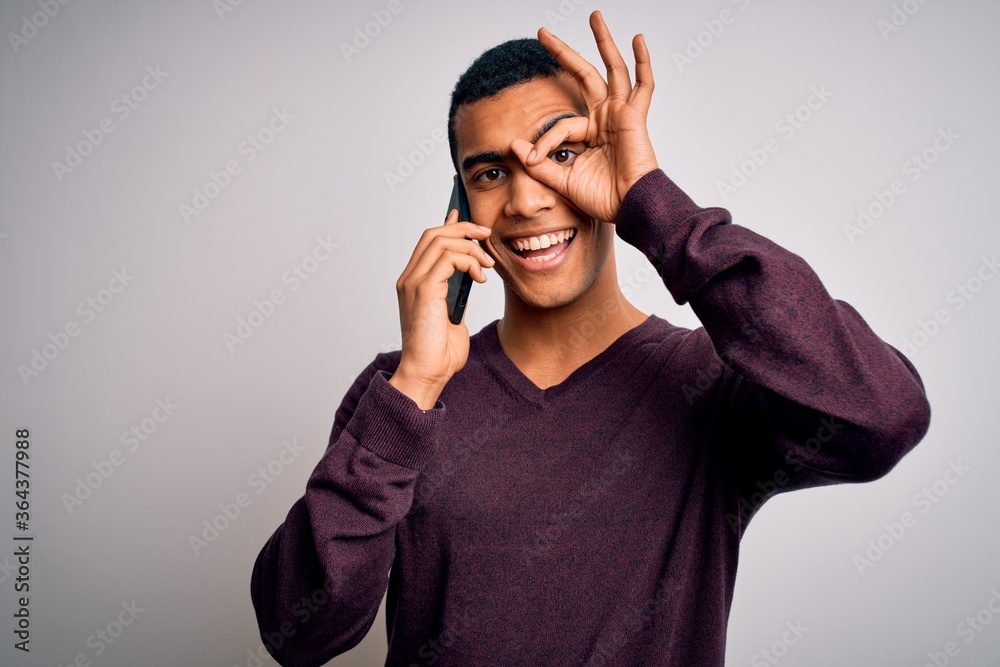 Young handsome african american man having conversation talking on the smartphone with happy face smiling doing ok sign with hand on eye looking through fingers