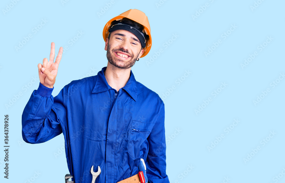 Young hispanic man wearing worker uniform smiling looking to the camera showing fingers doing victory sign. number two. Young hispanic man wearing worker uniform smiling looking to the camera showing fingers doing victory sign. number two.