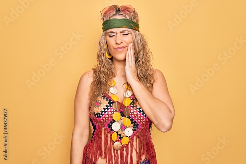Beautiful blonde hippie woman wearing sunglasses and accessories over yellow background touching mouth with hand with painful expression because of toothache or dental illness on teeth. Dentist