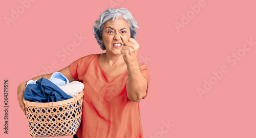 Canvastavla Senior woman with gray hair holding laundry basket annoyed and frustrated shouti
