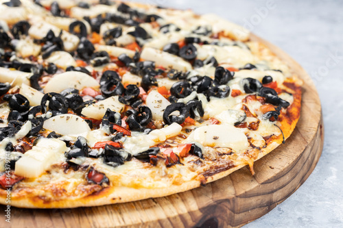 Close up of a pizza with black olives served on a rustic wooden board and set on a textured gray wooden background