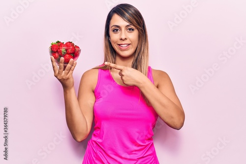 Young beautiful woman holding bowl with strawberries smiling happy pointing with hand and finger