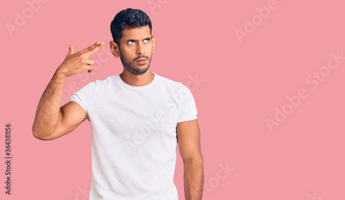 Photography Young latin man wearing casual clothes shooting and killing oneself pointing hand and fingers to head like gun, suicide gesture