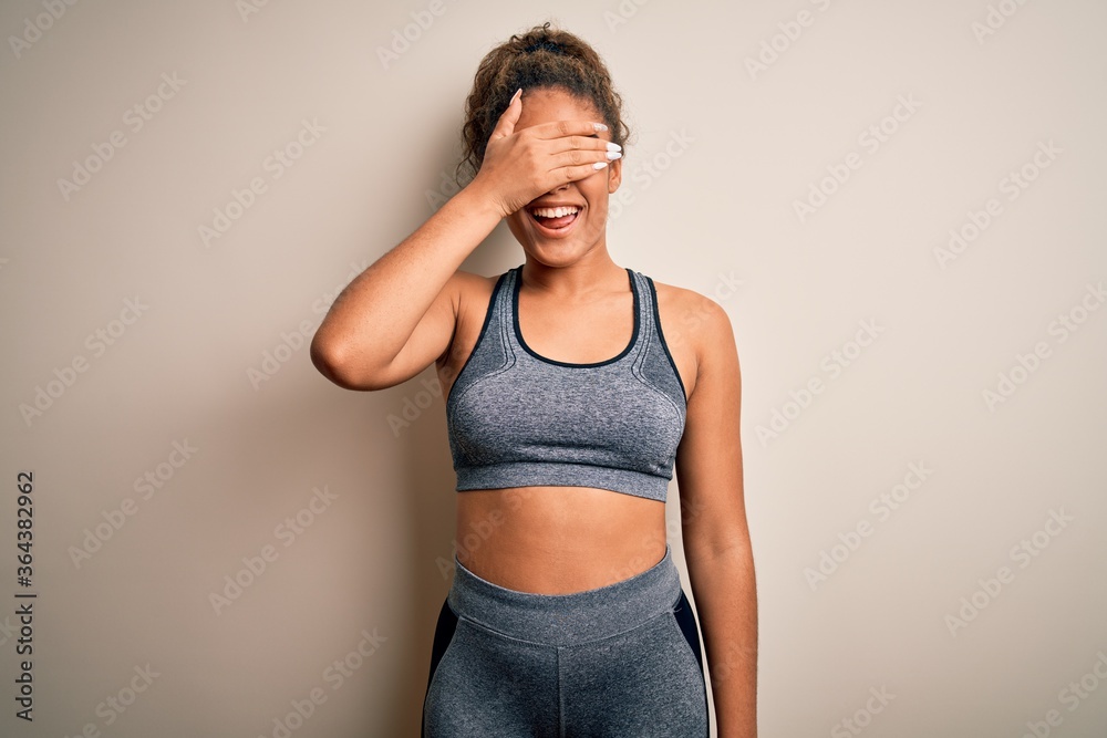 Young african american sportswoman doing sport wearing sportswear over white background smiling and laughing with hand on face covering eyes for surprise. Blind concept.