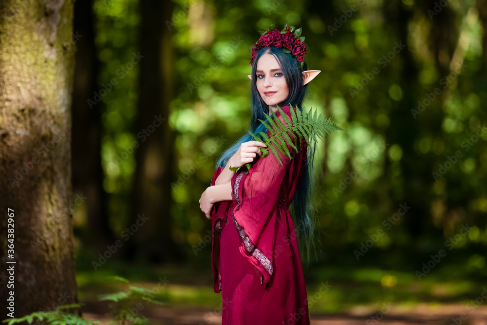 Costume Play Ideas. Forest Sprite in Flowery Garland Posing with Elf Enlarged Ears in Summer Forest With Fern Leaves.