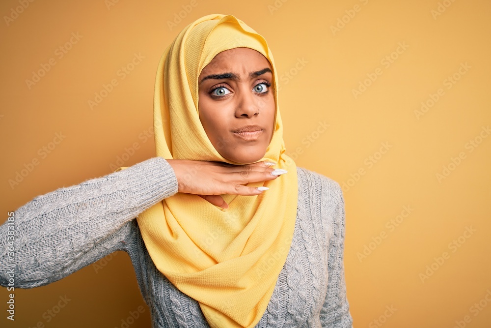Young beautiful african american girl wearing muslim hijab over isolated yellow background cutting throat with hand as knife, threaten aggression with furious violence Young beautiful african american girl wearing muslim hijab over isolated yellow background cutting throat with hand as knife, threaten aggression with furious violence