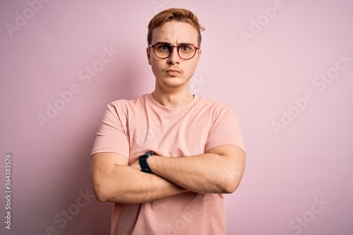 Young handsome redhead man wearing casual t-shirt standing over isolated pink background skeptic and nervous, disapproving expression on face with crossed arms. Negative person.