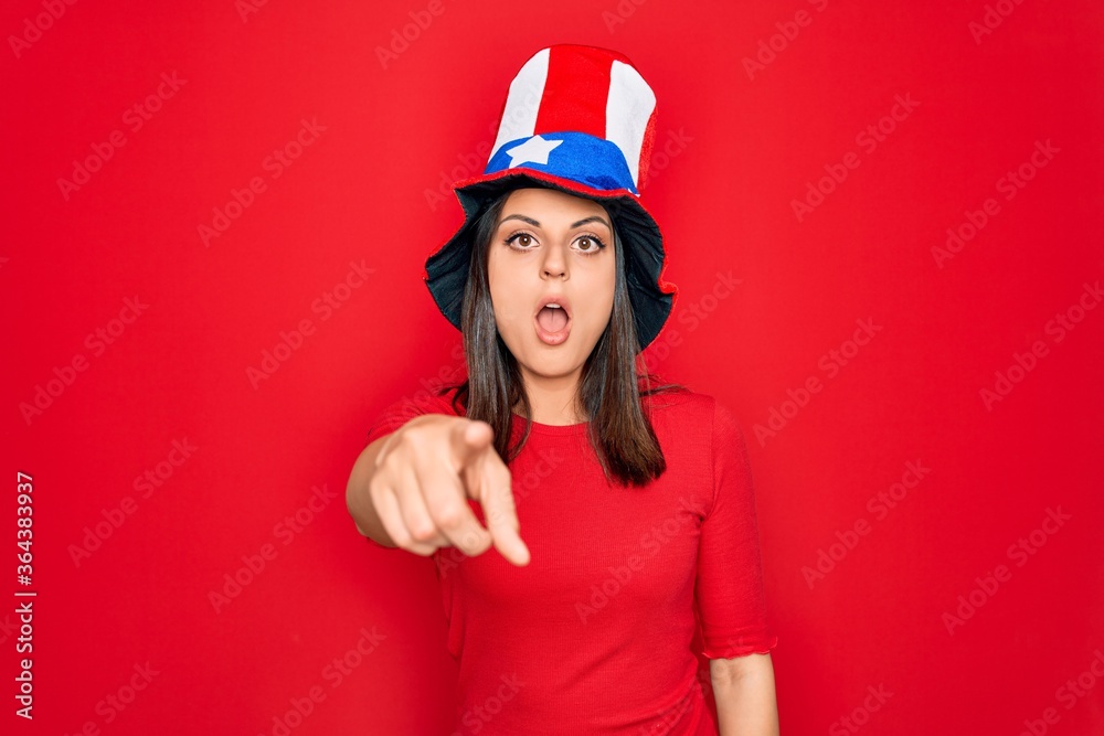 Young beautiful brunette woman wearing united states hat celebrating independence day pointing displeased and frustrated to the camera, angry and furious with you Young beautiful brunette woman wearing united states hat celebrating independence day pointing displeased and frustrated to the camera, angry and furious with you