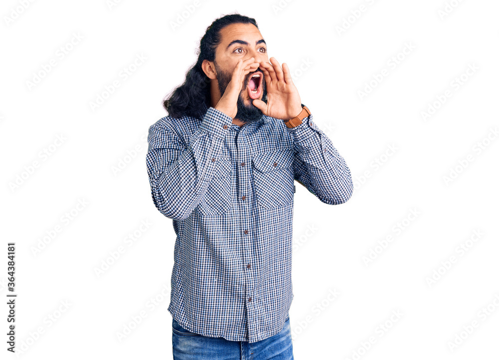 Young arab man wearing casual clothes shouting angry out loud with hands over mouth Young arab man wearing casual clothes shouting angry out loud with hands over mouth