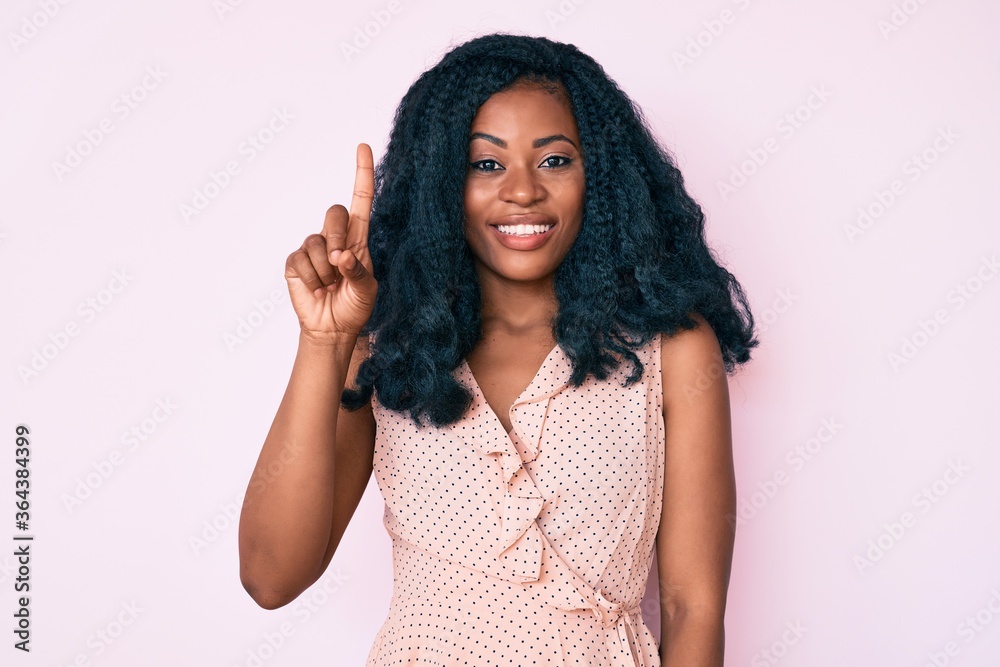 Beautiful african woman wearing casual summer clothes smiling with an idea or question pointing finger up with happy face, number one