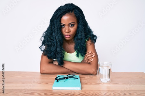 Beautiful african woman sitting on the table stuying for university skeptic and nervous, disapproving expression on face with crossed arms. negative person. photo