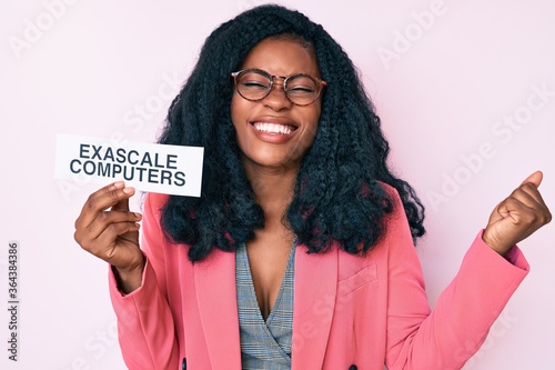 Beautiful african woman holding exascale computers banner screaming proud, celebrating victory and success very excited with raised arm photo