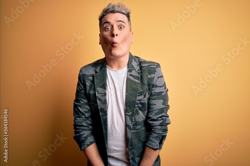 Young handsome modern man wearing business jacket standing over yellow isolated background making fish face with lips, crazy and comical gesture. Funny expression.