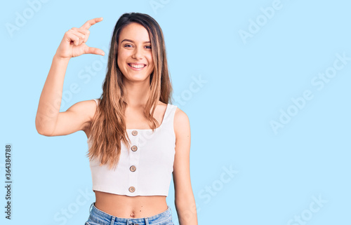Young beautiful girl wearing casual sleeveless t shirt smiling and confident gesturing with hand doing small size sign with fingers looking and the camera. measure concept.