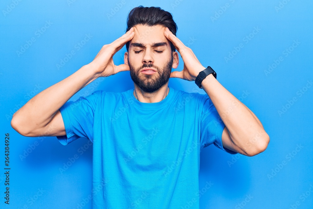 Young handsome man with beard wearing casual t-shirt with hand on head, headache because stress. suffering migraine. Young handsome man with beard wearing casual t-shirt with hand on head, headache because stress. suffering migraine.