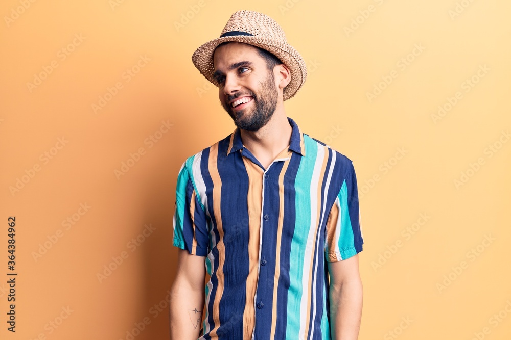 Young handsome man with beard wearing summer hat and shirt looking away to side with smile on face, natural expression. laughing confident. Young handsome man with beard wearing summer hat and shirt looking away to side with smile on face, natural expression. laughing confident.