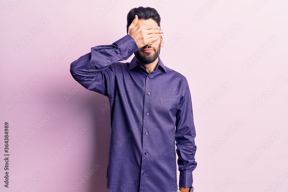 Young handsome man with beard wearing casual shirt covering eyes with hand, looking serious and sad. sightless, hiding and rejection concept Young handsome man with beard wearing casual shirt covering eyes with hand, looking serious and sad. sightless, hiding and rejection concept
