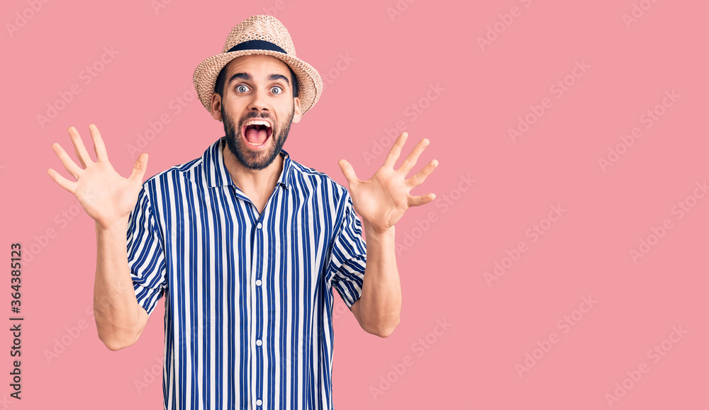 Naklejka premium Young handsome man with beard wearing summer hat and striped shirt celebrating crazy and amazed for success with arms raised and open eyes screaming excited. winner concept
