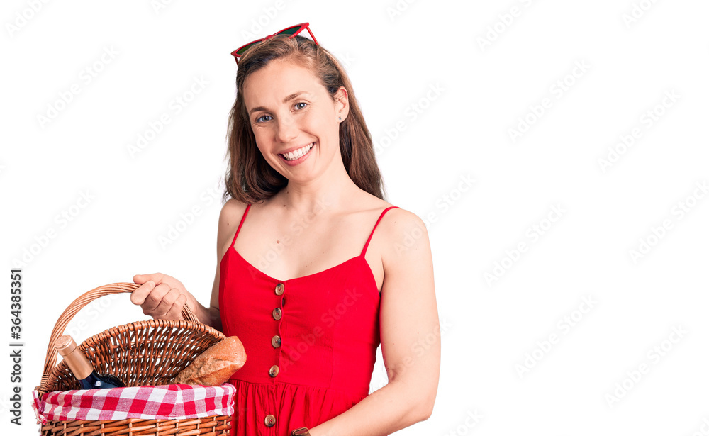 Young beautiful blonde woman holding picnic basket looking positive and happy standing and smiling with a confident smile showing teeth Young beautiful blonde woman holding picnic basket looking positive and happy standing and smiling with a confident smile showing teeth