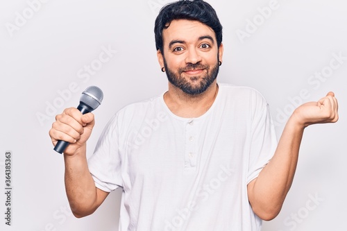 Young hispanic man singing song using microphone screaming proud, celebrating victory and success very excited with raised arm