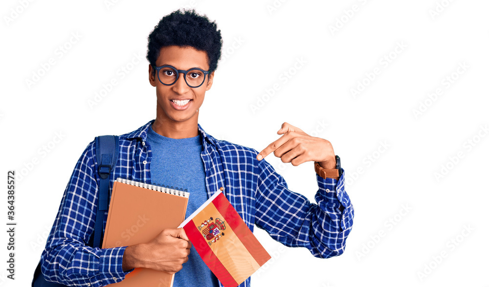 Young african american man wearing student backpack holding spanish flag smiling happy pointing with hand and finger Young african american man wearing student backpack holding spanish flag smiling happy pointing with hand and finger