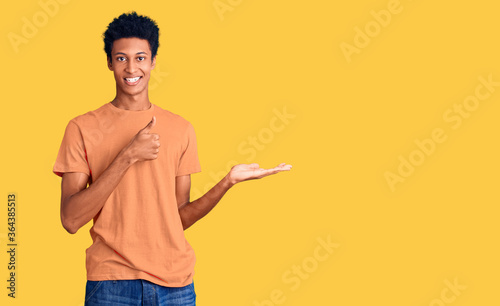 Young african american man wearing casual clothes showing palm hand and doing ok gesture with thumbs up, smiling happy and cheerful