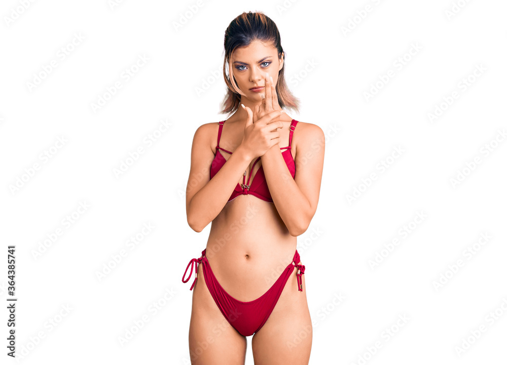 Fototapeta premium Young beautiful woman wearing bikini holding symbolic gun with hand gesture, playing killing shooting weapons, angry face
