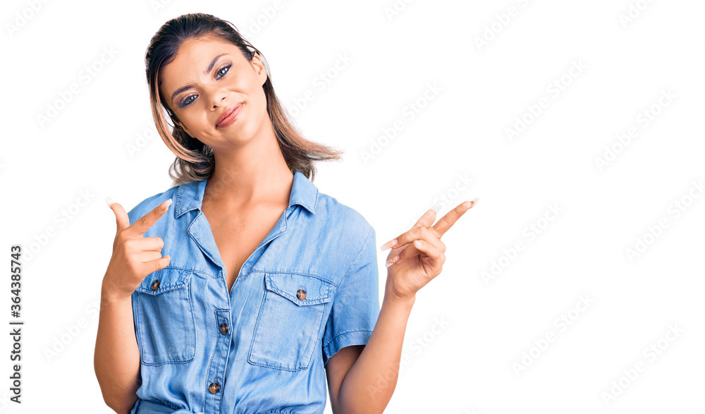 Young beautiful woman wearing casual clothes smiling and looking at the camera pointing with two hands and fingers to the side.