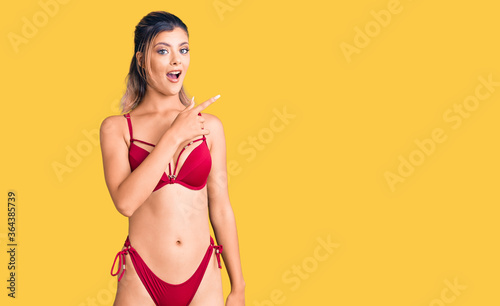 Young beautiful woman wearing bikini surprised pointing with finger to the side, open mouth amazed expression.