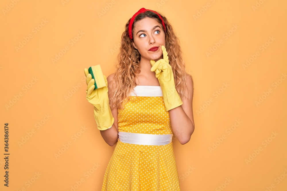 Young beautiful blonde woman with blue eyes cleaning using gloves and cleaner scourer serious face thinking about question, very confused idea Young beautiful blonde woman with blue eyes cleaning using gloves and cleaner scourer serious face thinking about question, very confused idea