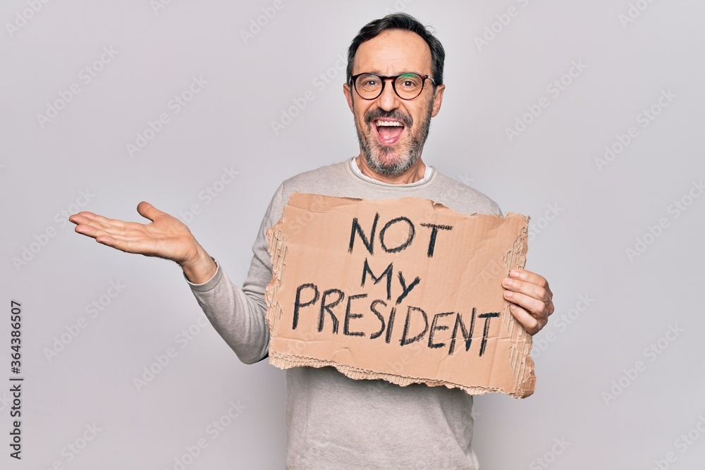 Middle age handsome man on disagreement holding banner with not my president message celebrating achievement with happy smile and winner expression with raised hand Middle age handsome man on disagreement holding banner with not my president message celebrating achievement with happy smile and winner expression with raised hand