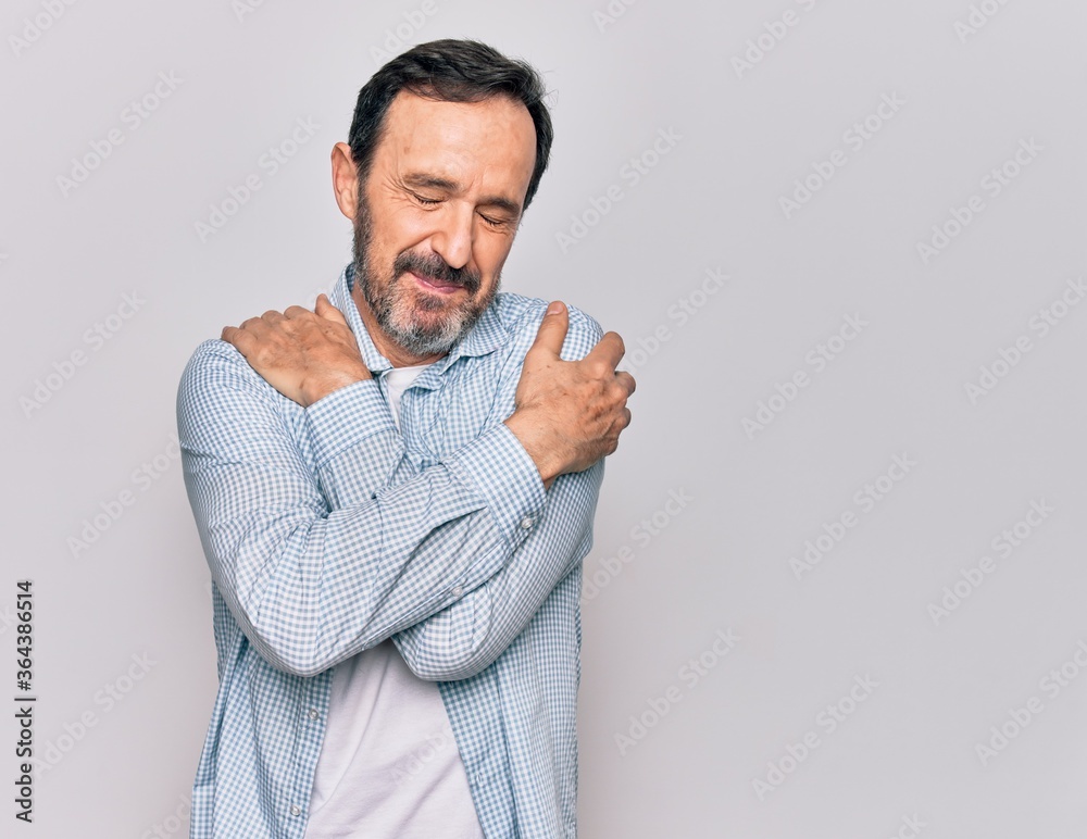 Middle age handsome man wearing casual denim shirt standing over isolated white background hugging oneself happy and positive, smiling confident. Self love and self care