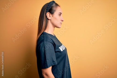 Young beautiful woman wearing volunteer t-shirt doing volunteering over yellow background looking to side, relax profile pose with natural face and confident smile.