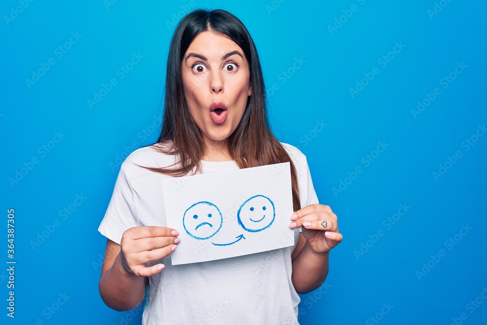 Woman asking for psychology change holding paper with unhappy to happy emotion message scared and amazed with open mouth for surprise, disbelief face Woman asking for psychology change holding paper with unhappy to happy emotion message scared and amazed with open mouth for surprise, disbelief face