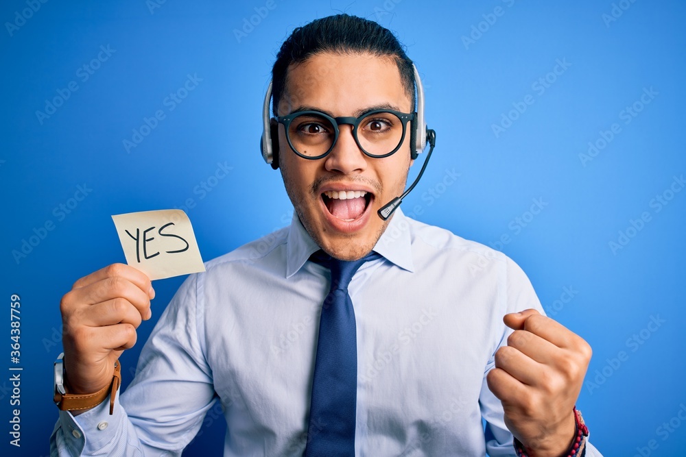 Young brazilian call center agent man holding reminder paper with yes message screaming proud and celebrating victory and success very excited, cheering emotion Young brazilian call center agent man holding reminder paper with yes message screaming proud and celebrating victory and success very excited, cheering emotion