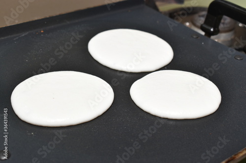 circular round utappam made up of white batter on hot non stick pan