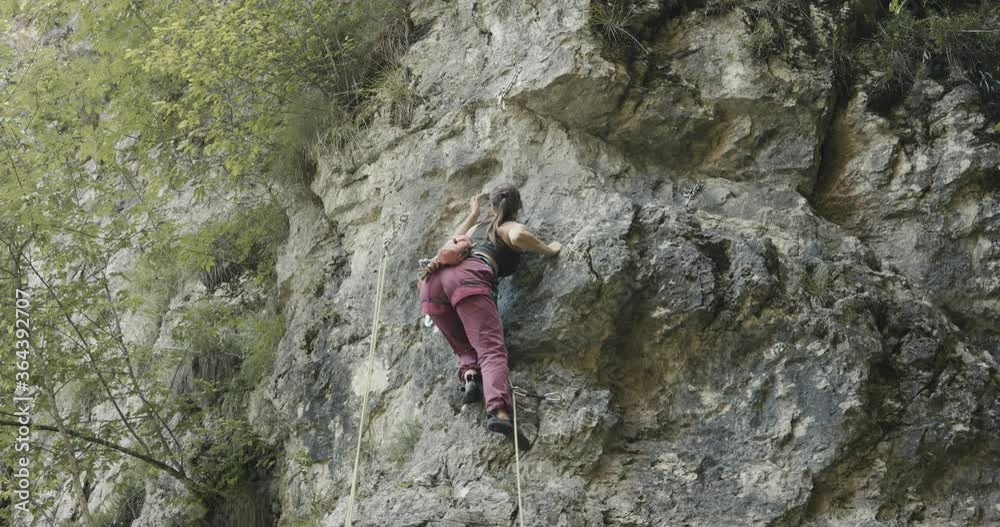 Female paralympic climber woman athlete with missing fingers on left hand finish rock climb reaches top attach carabiner rope outdoors lifestyle sport in nature Female paralympic climber woman athlete with missing fingers on left hand finish rock climb reaches top attach carabiner rope outdoors lifestyle sport in nature
