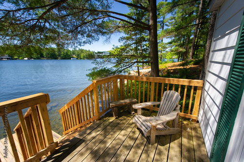 Fotografering Adirondack chair sitting on a cottage wooden deck facing a calm lake during a summer day in Muskoka, Ontario Canada