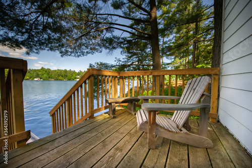 Fototapeta Adirondack chair sitting on a cottage wooden deck facing a calm lake during a summer day in Muskoka, Ontario Canada