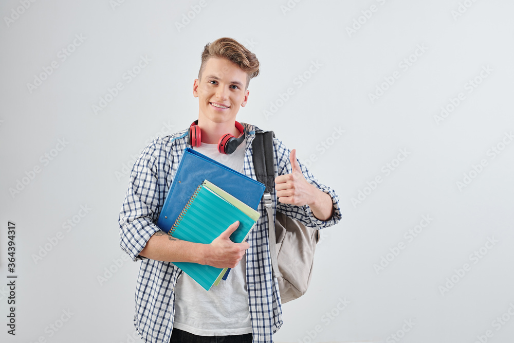 Portrait of happy handsome young high school student with textbooks showing thumbs-up and smiling at camera Portrait of happy handsome young high school student with textbooks showing thumbs-up and smiling at camera