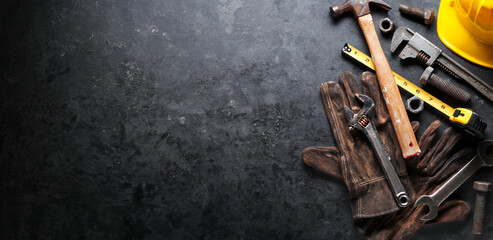 Hardhat, hammer, wrench, gloves, and other worn and dirty tools on dark background with copy space. Father's day, DIY, home improvement, or labor day background concept.